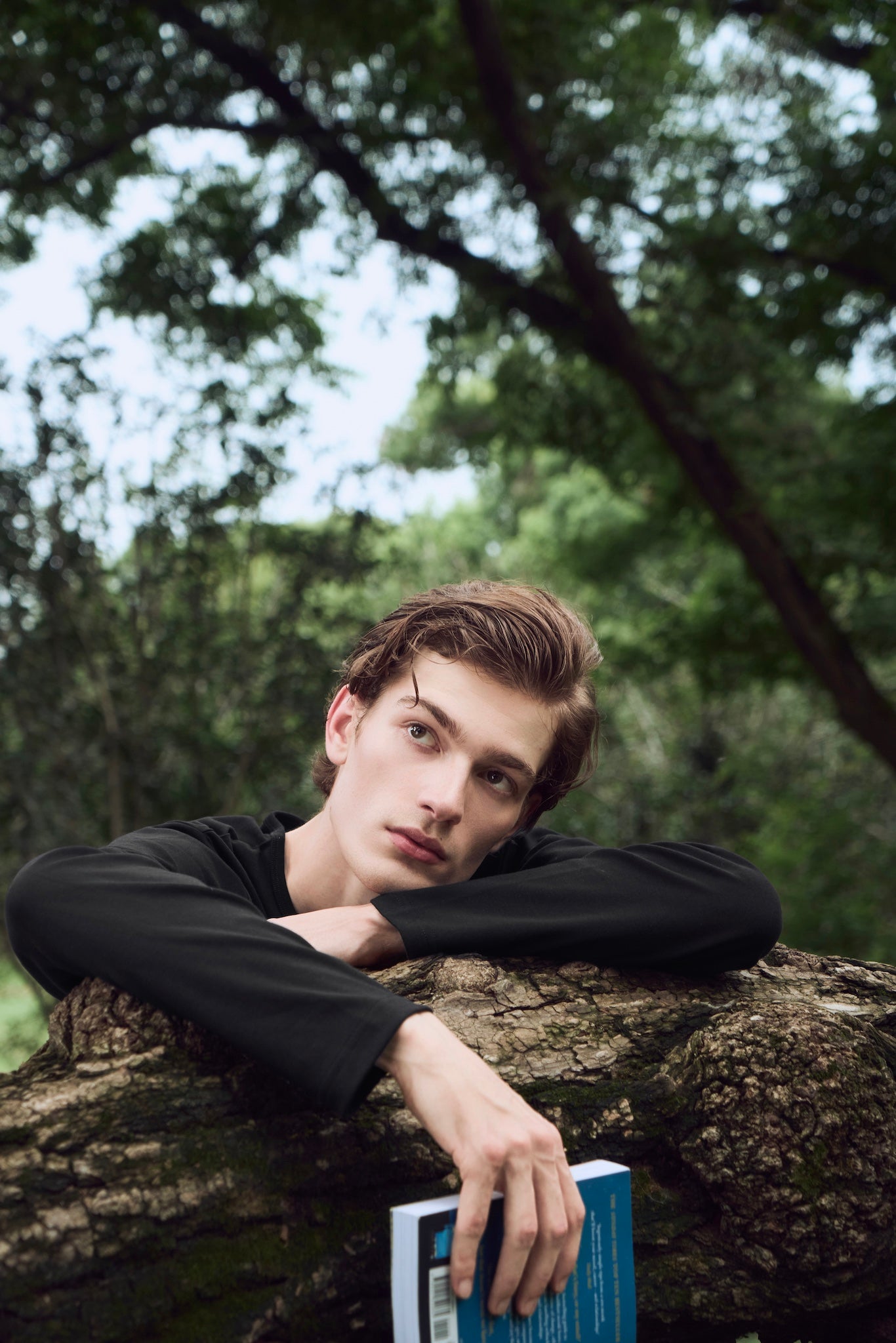 Male model holding a book, looking thoughtfully into the distance, wearing AURETEMPHE black organic cotton long sleeve t-shirt.