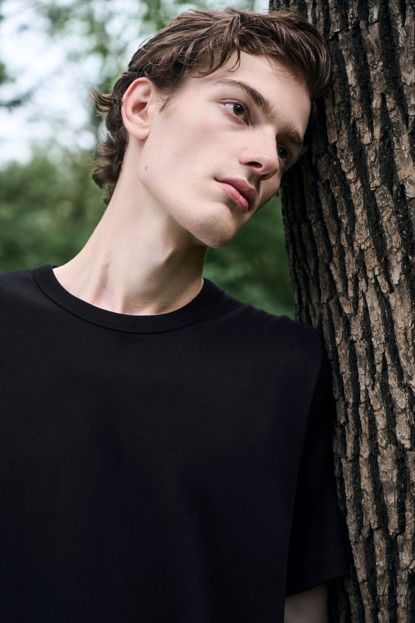 Male model leaning his head against a tree, deep in thought, wearing AURETEMPHE black organic cotton long sleeve t-shirt.