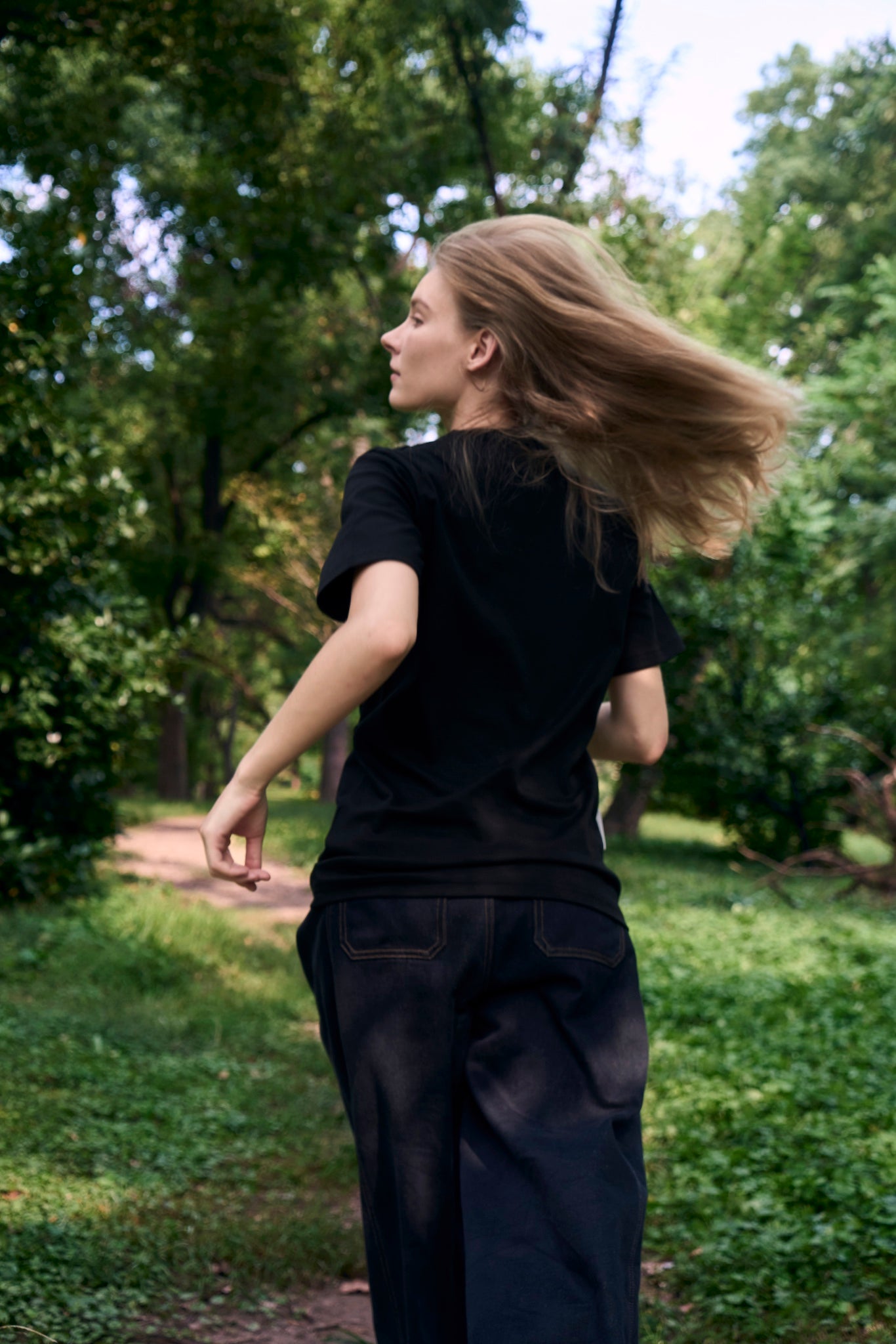 Female model running lightly along a forest path, wearing AURETEMPHE black organic cotton short sleeve t-shirt.