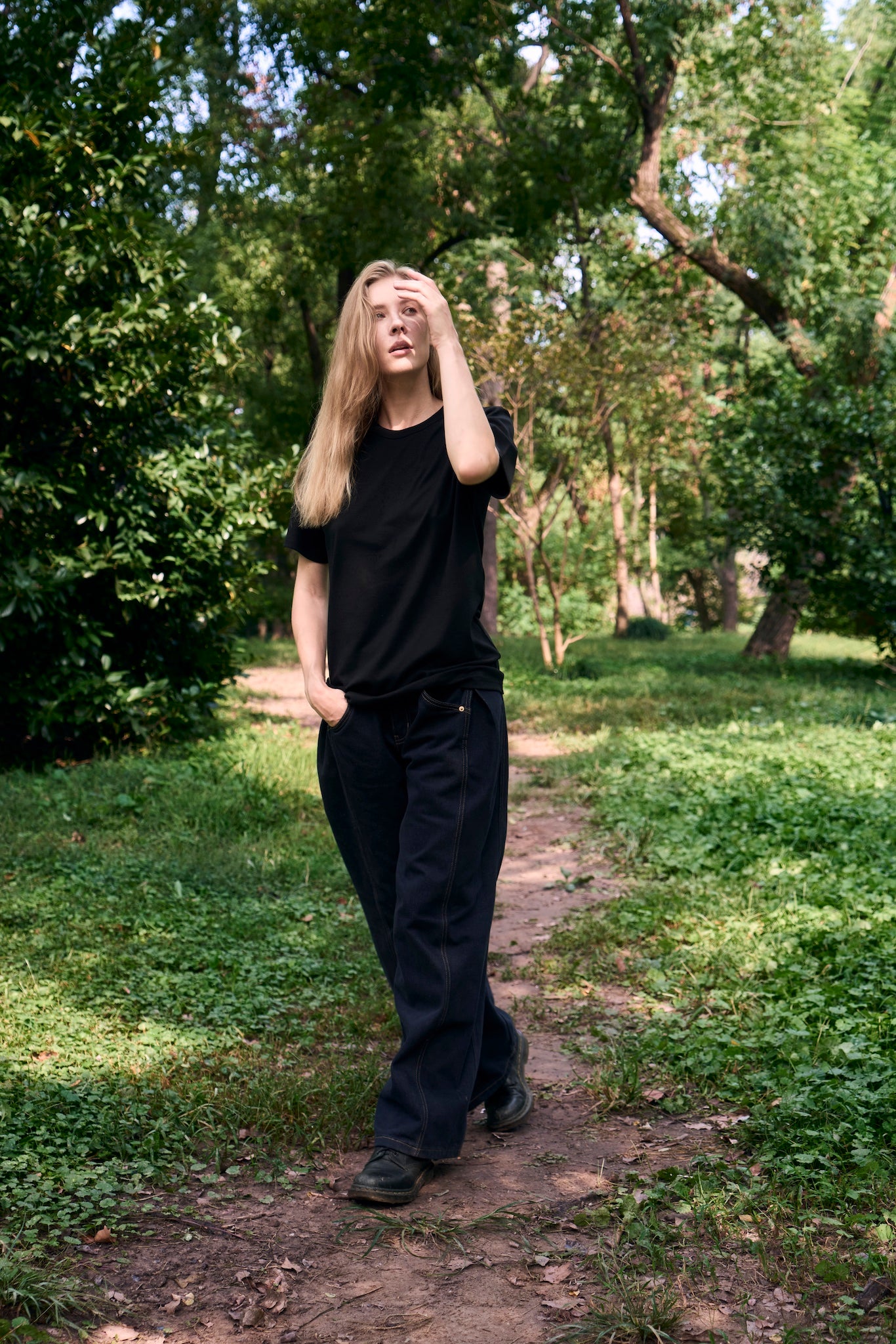 Female model walking along a forest path, exploring her surroundings, wearing AURETEMPHE black organic cotton short sleeve t-shirt.
