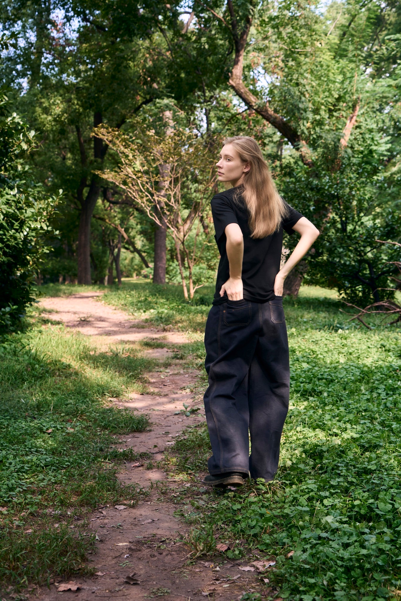 Female model walking along a forest path, looking back, wearing AURETEMPHE black organic cotton short sleeve t-shirt.