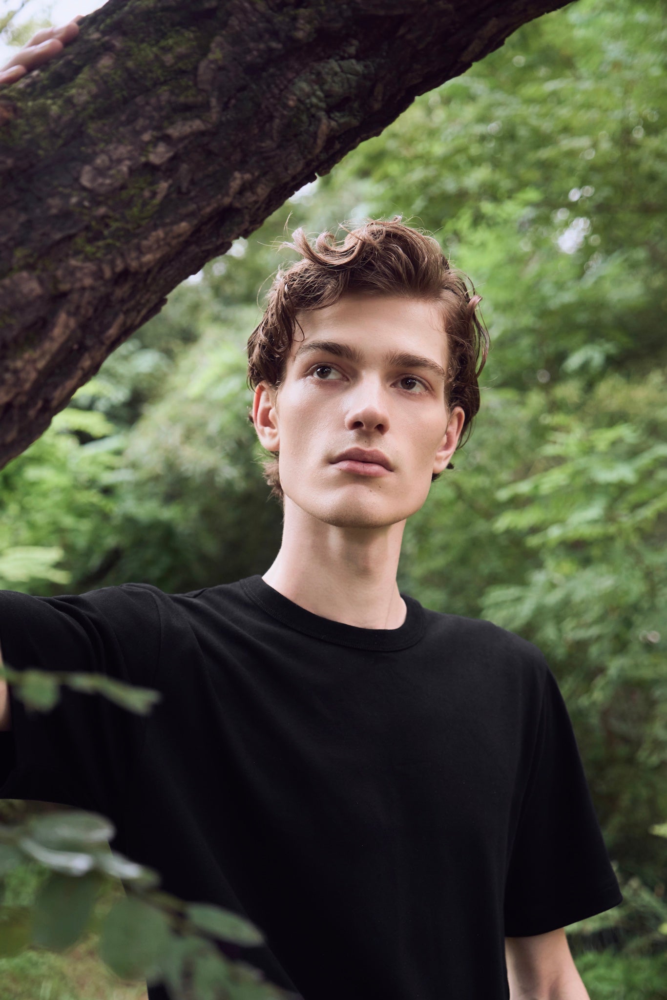 Male model exploring in nature, appearing to have discovered something, wearing AURETEMPHE black organic cotton long sleeve t-shirt.