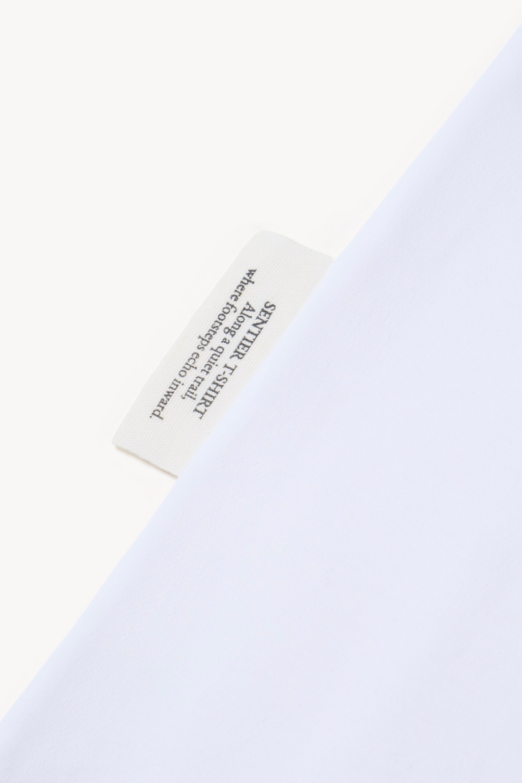 Detail of AURETEMPHE white short sleeve t-shirt showing its organic cotton side label.