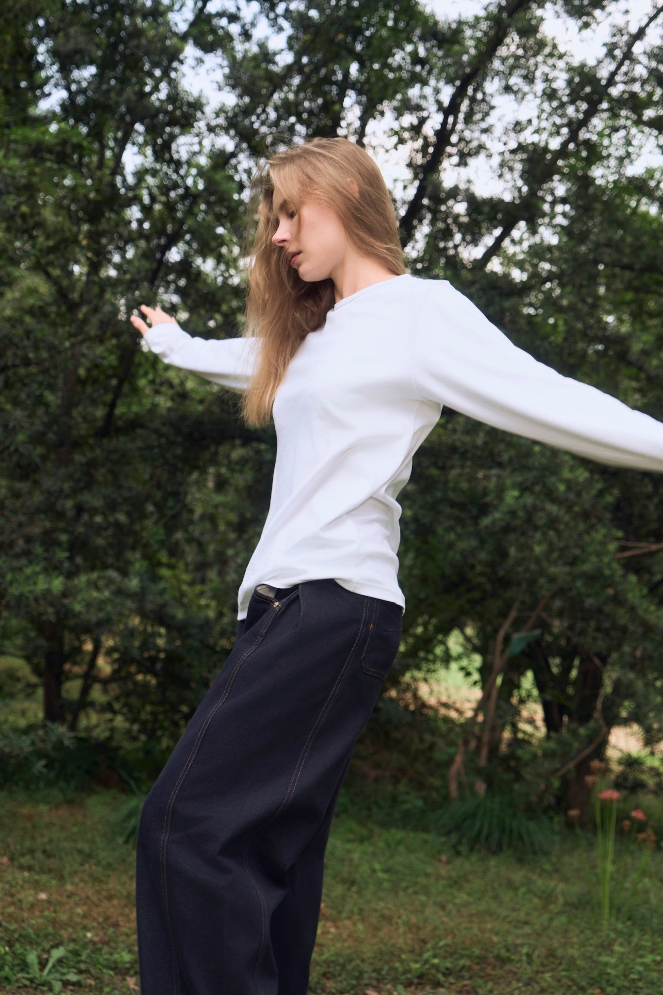 Female model exploring a clearing in the forest, wearing AURETEMPHE white organic cotton long sleeve t-shirt.