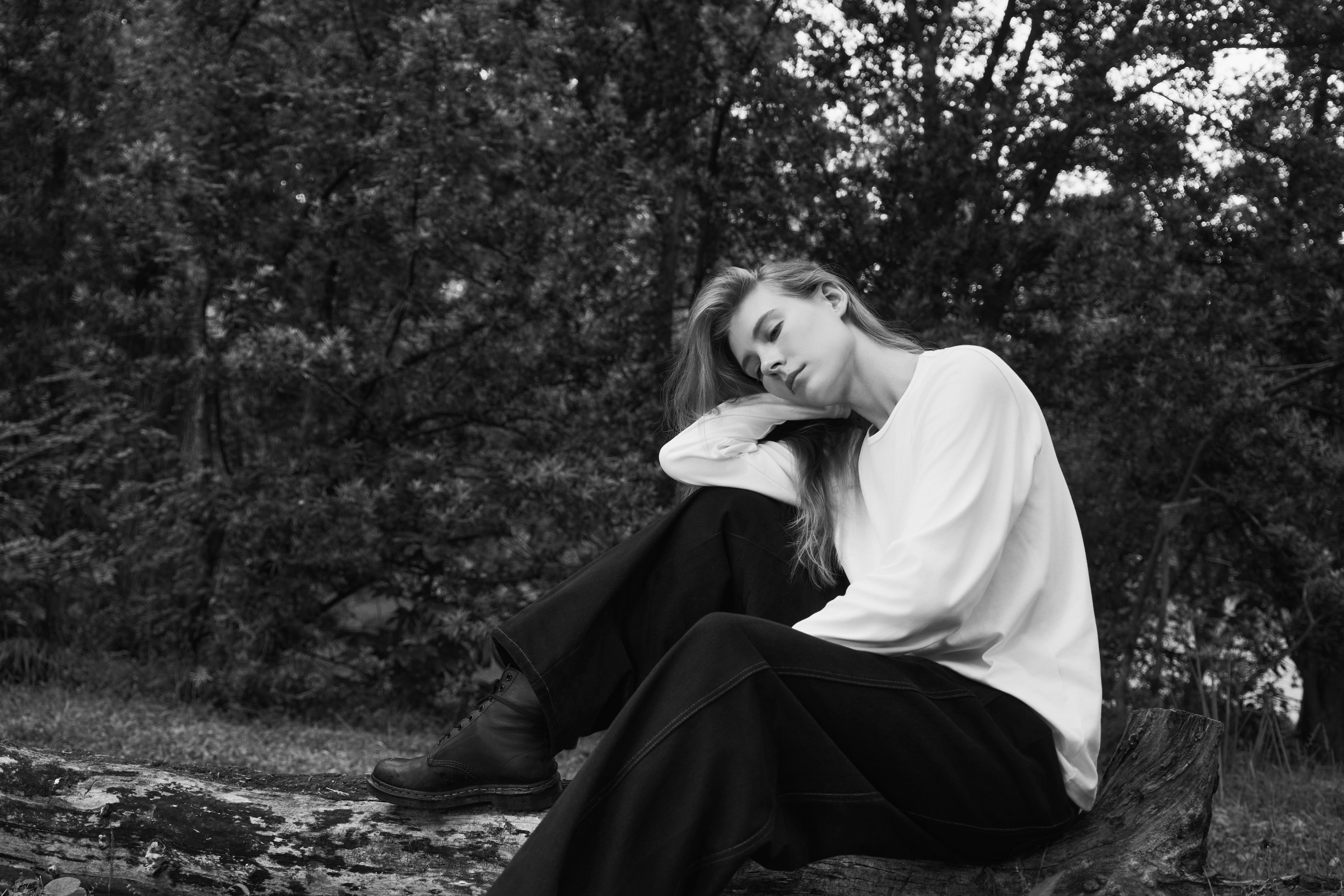 Female model sitting in nature with eyes closed, wearing AURETEMPHE white organic cotton long sleeve t-shirt.