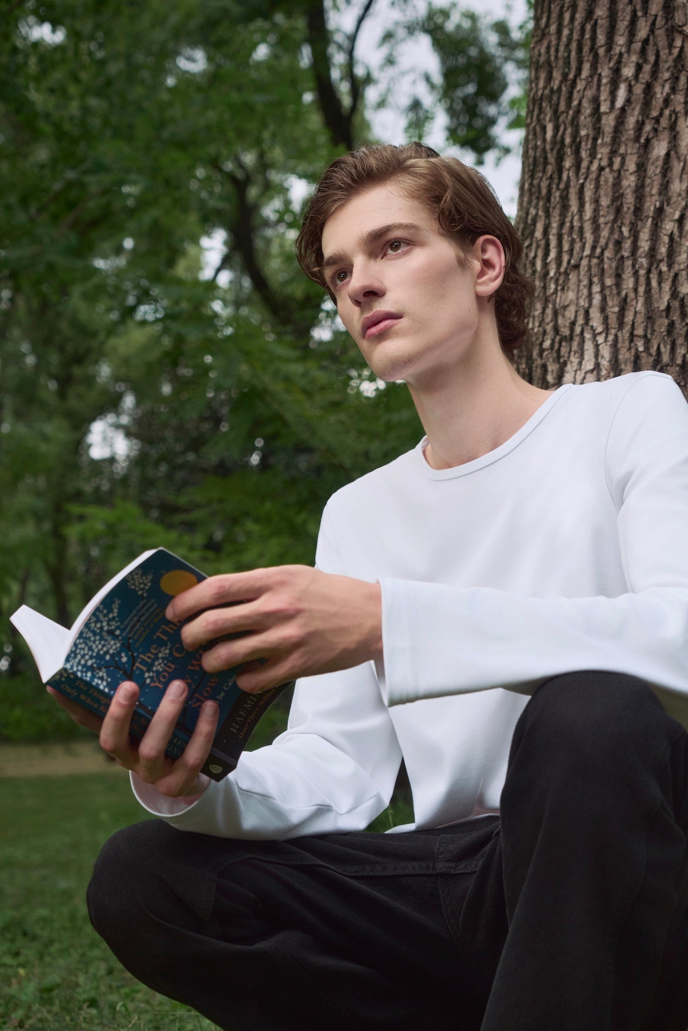 Male model holding a book, looking pensively toward the horizon, wearing AURETEMPHE white organic cotton long sleeve t-shirt.