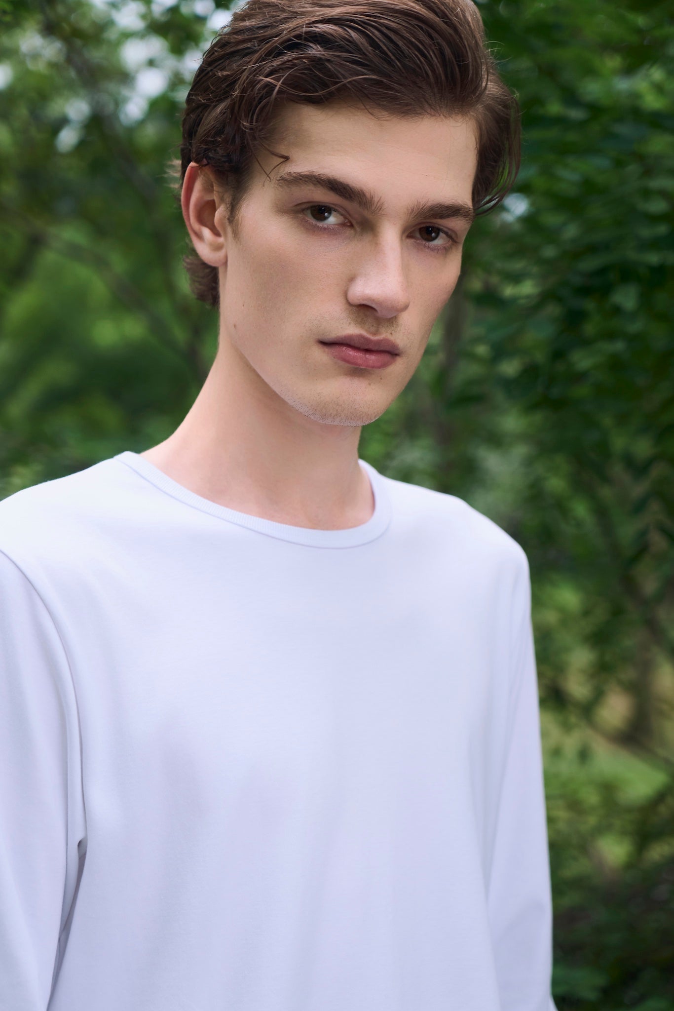 Male model looking straight ahead with a calm expression, wearing AURETEMPHE white organic cotton long sleeve t-shirt.
