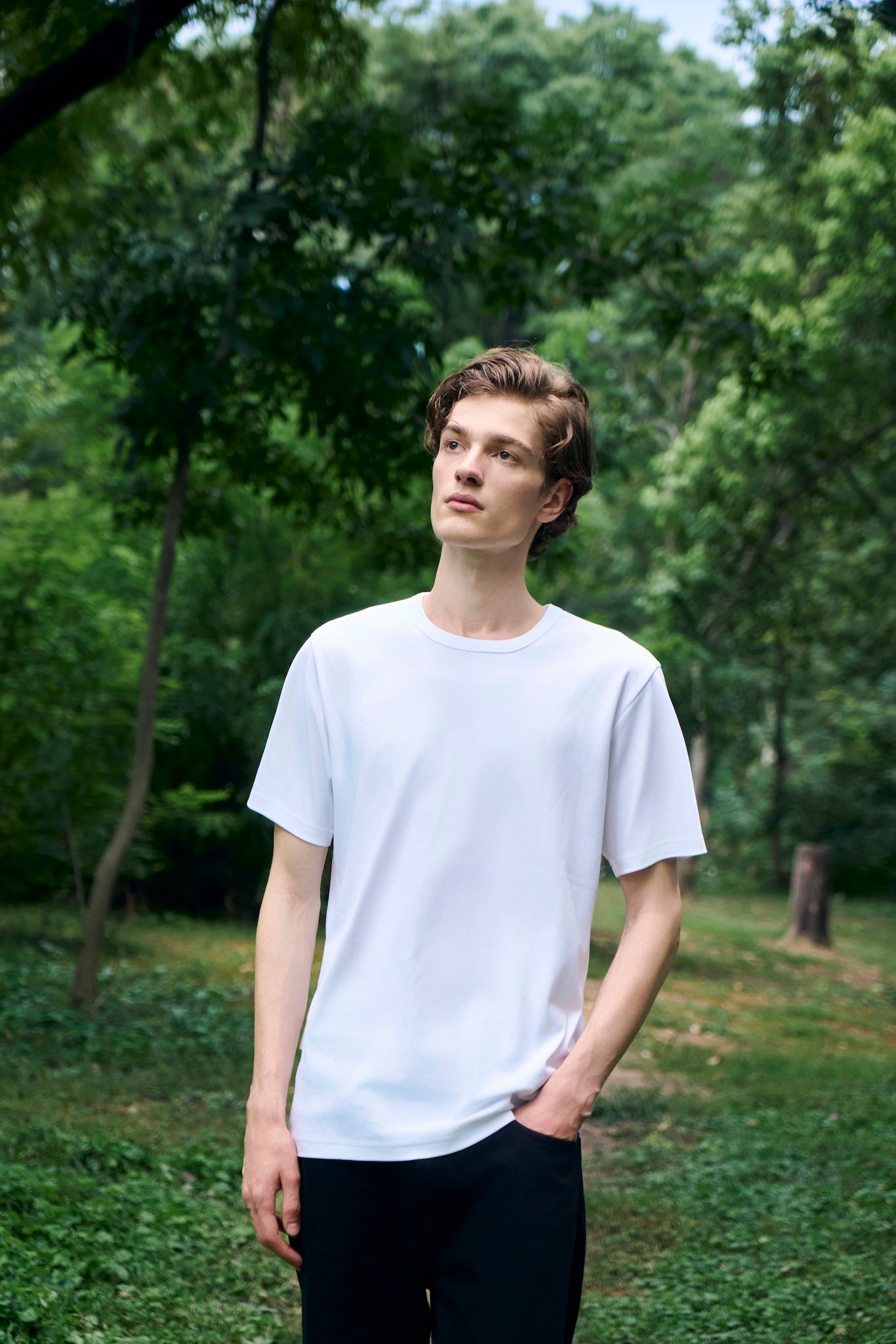 Male model walking along a forest path, freely exploring the surroundings, wearing AURETEMPHE white organic cotton short sleeve t-shirt.